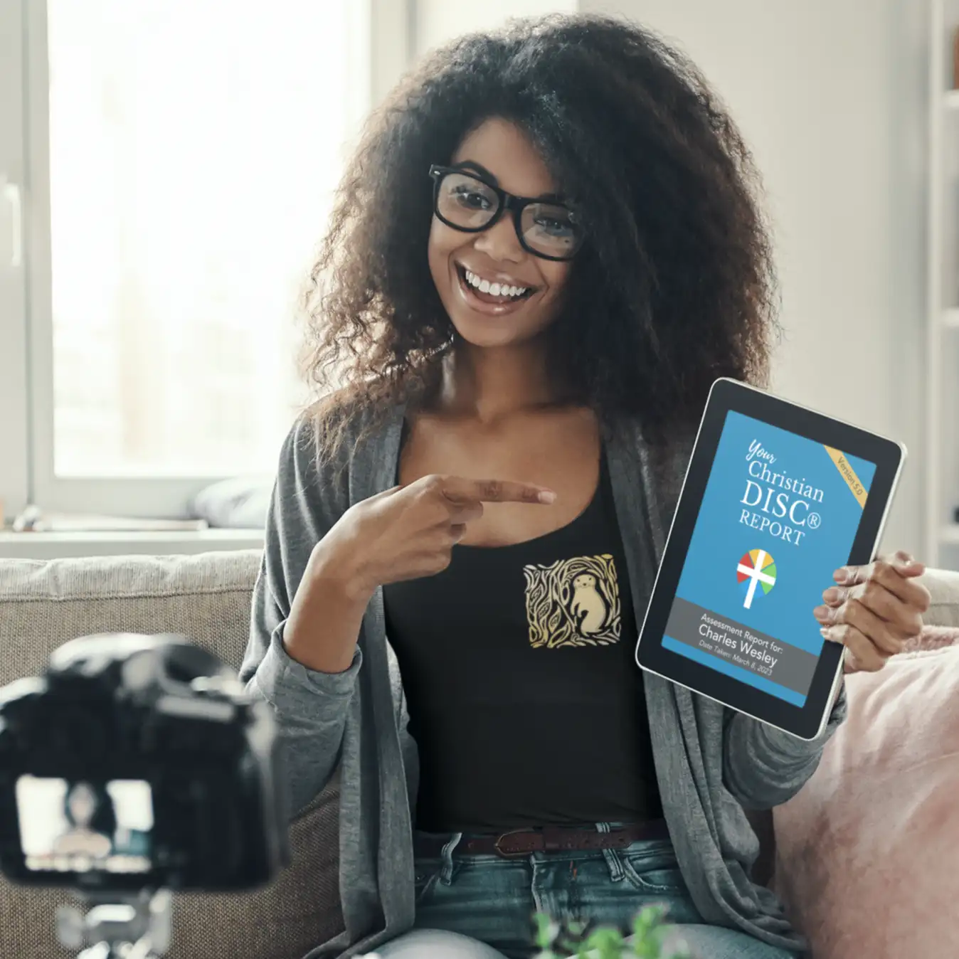 Black tablet displaying a blue ’your christian disc report’ screen with white and yellow text, held by a woman in front of a camera.