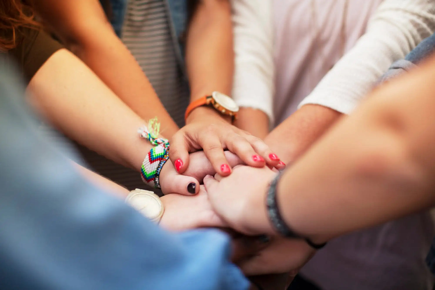 Hands clasped together in a circle, adorned with colorful woven bracelets and nail polish.