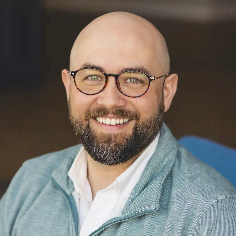 A man with a bald head and full beard wearing round black-framed glasses.