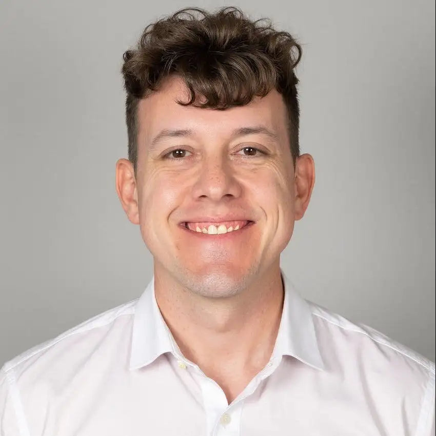 A man with curly brown hair wearing a crisp white button-down shirt.