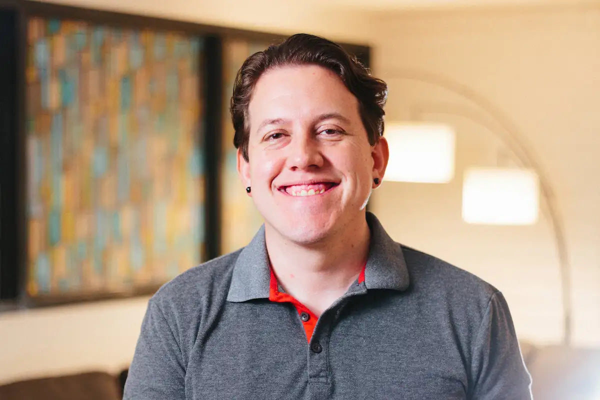 A smiling man wearing a gray polo shirt with red inner collar.
