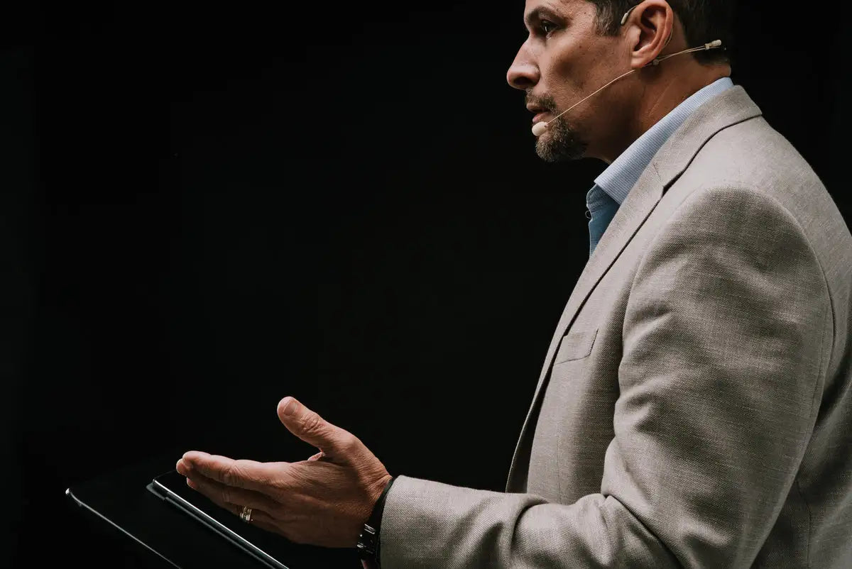 A man in a light gray suit jacket over a blue collared shirt, holding a black tablet.