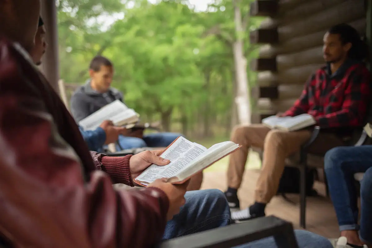 Open bible with red leather binding held by a person in a maroon jacket.