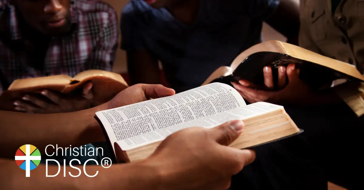 Open hardcover bible with cream-colored pages and dark binding, held by hands in a group setting.