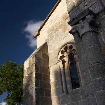 The stone facade of the ancient church features a weathered, light beige stonework with intricate carved columns and an arched window.
