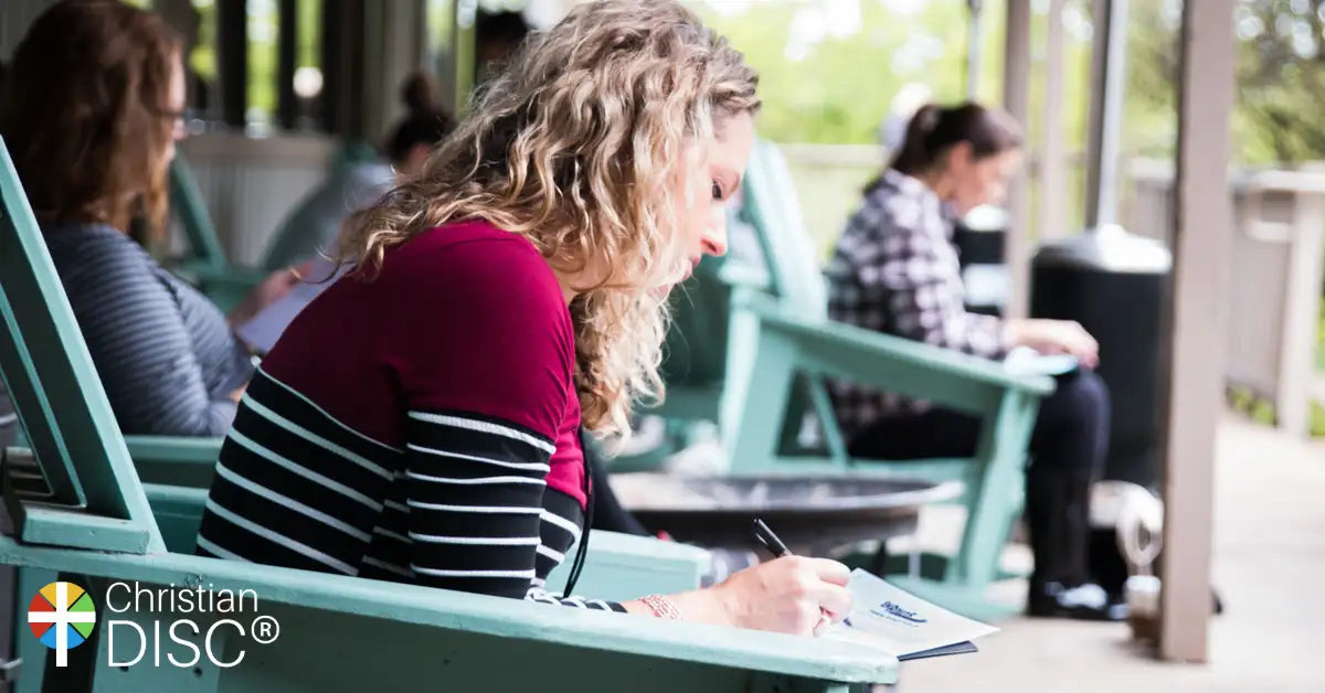 A woman with curly blonde hair sits in a teal wooden adirondack chair, wearing a maroon and black striped long-sleeve top.