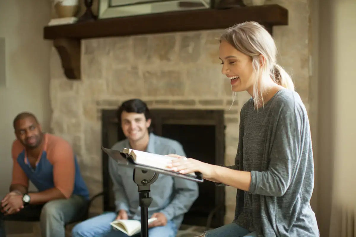 A woman in a gray long-sleeved top smiles while holding an open book on a stand.