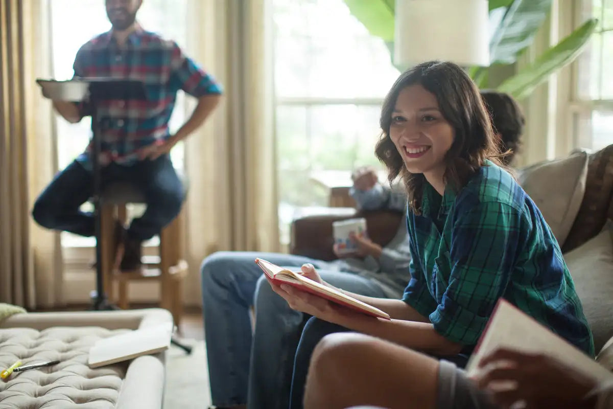 Woman in green and blue plaid shirt sitting on couch holding open book